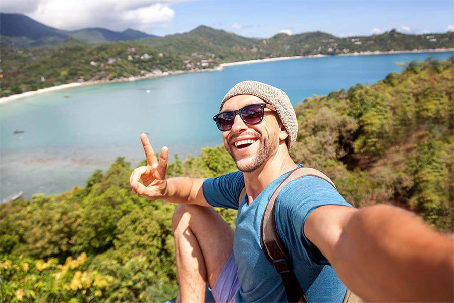 Smiling man with sunglasses taking a selfie with the lake behind him